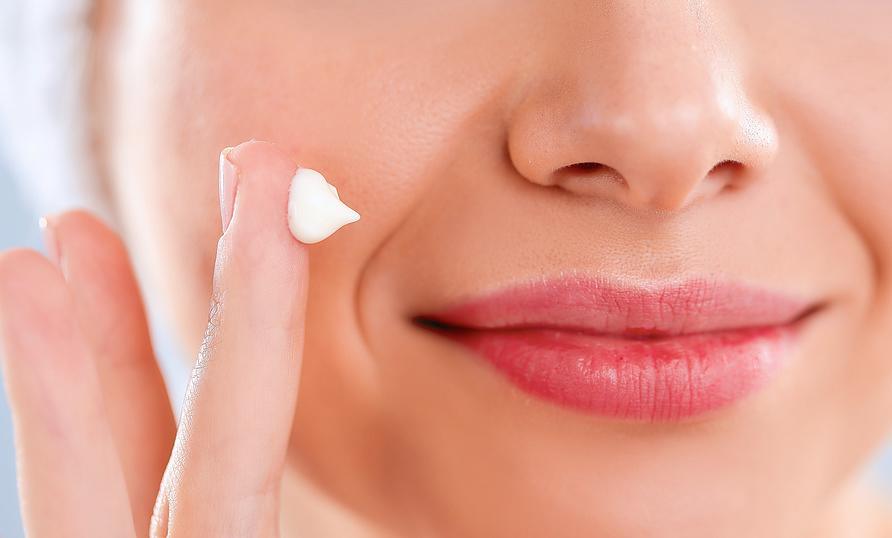 Beautiful Young Woman Applying A Creme On Her Face Isolated On Gray Background.